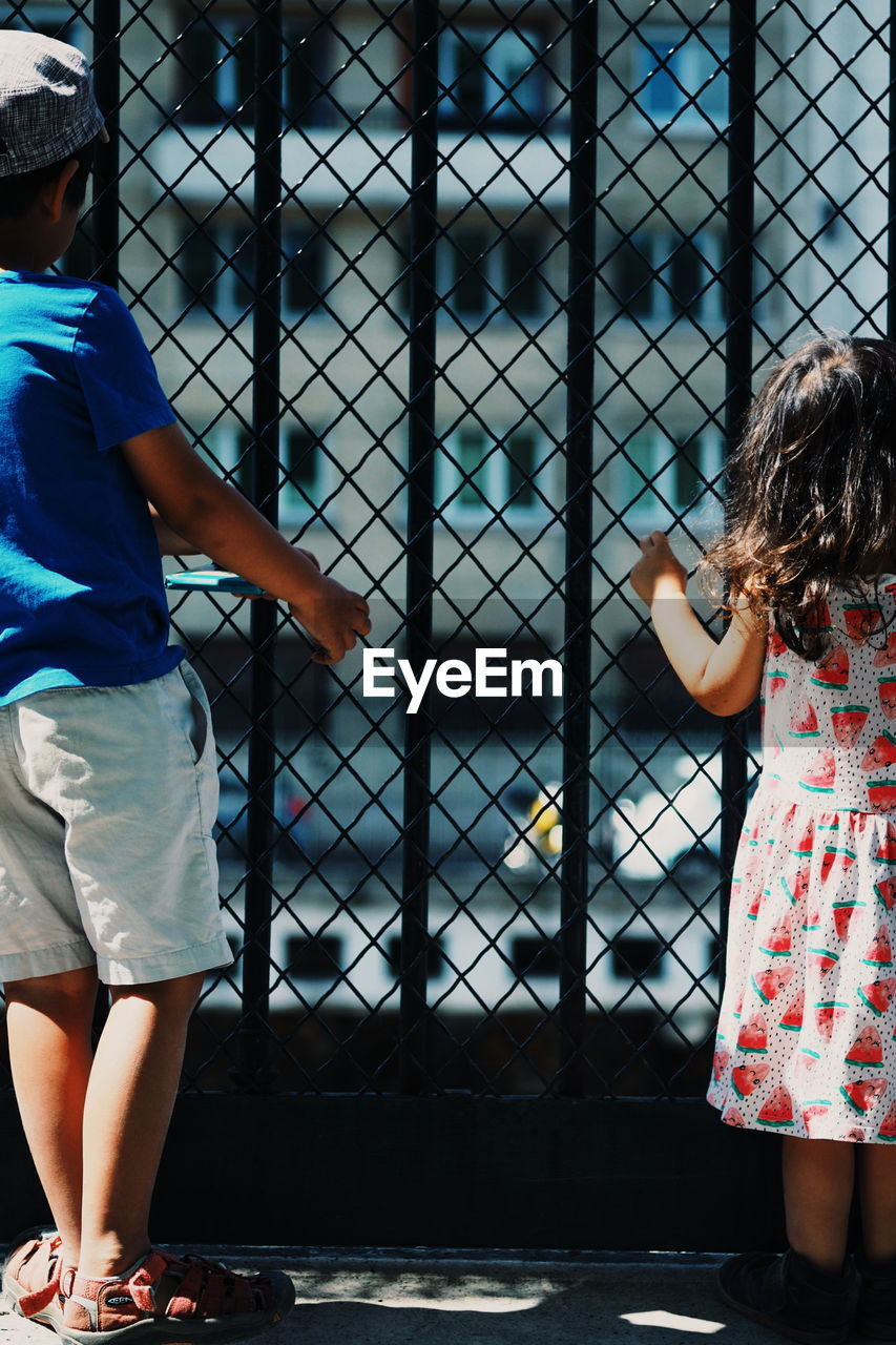 Two children looking out through fenced gate