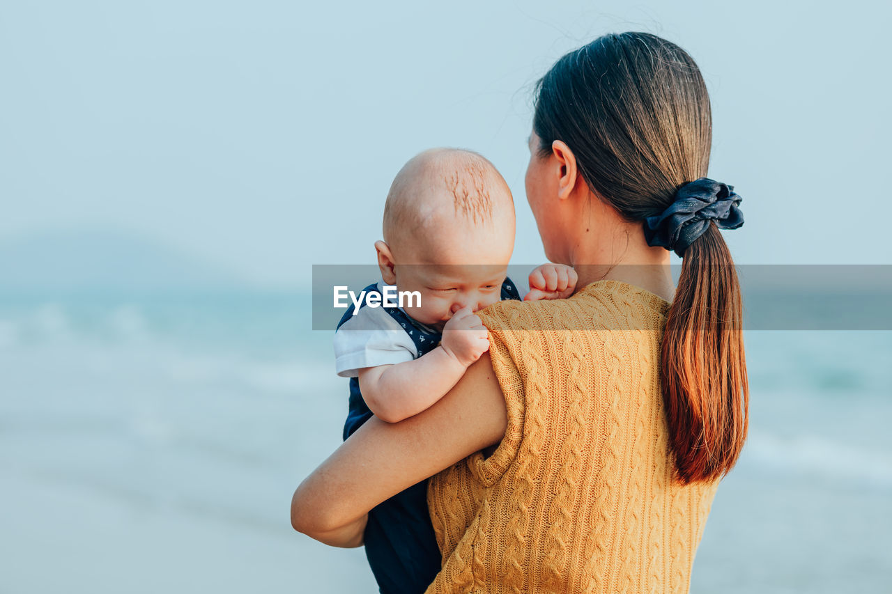 Mother and daughter by sea against clear sky