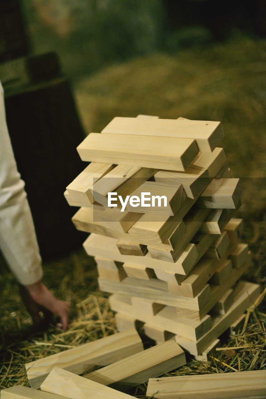 Cropped hand of person by stacked wooden blocks on field