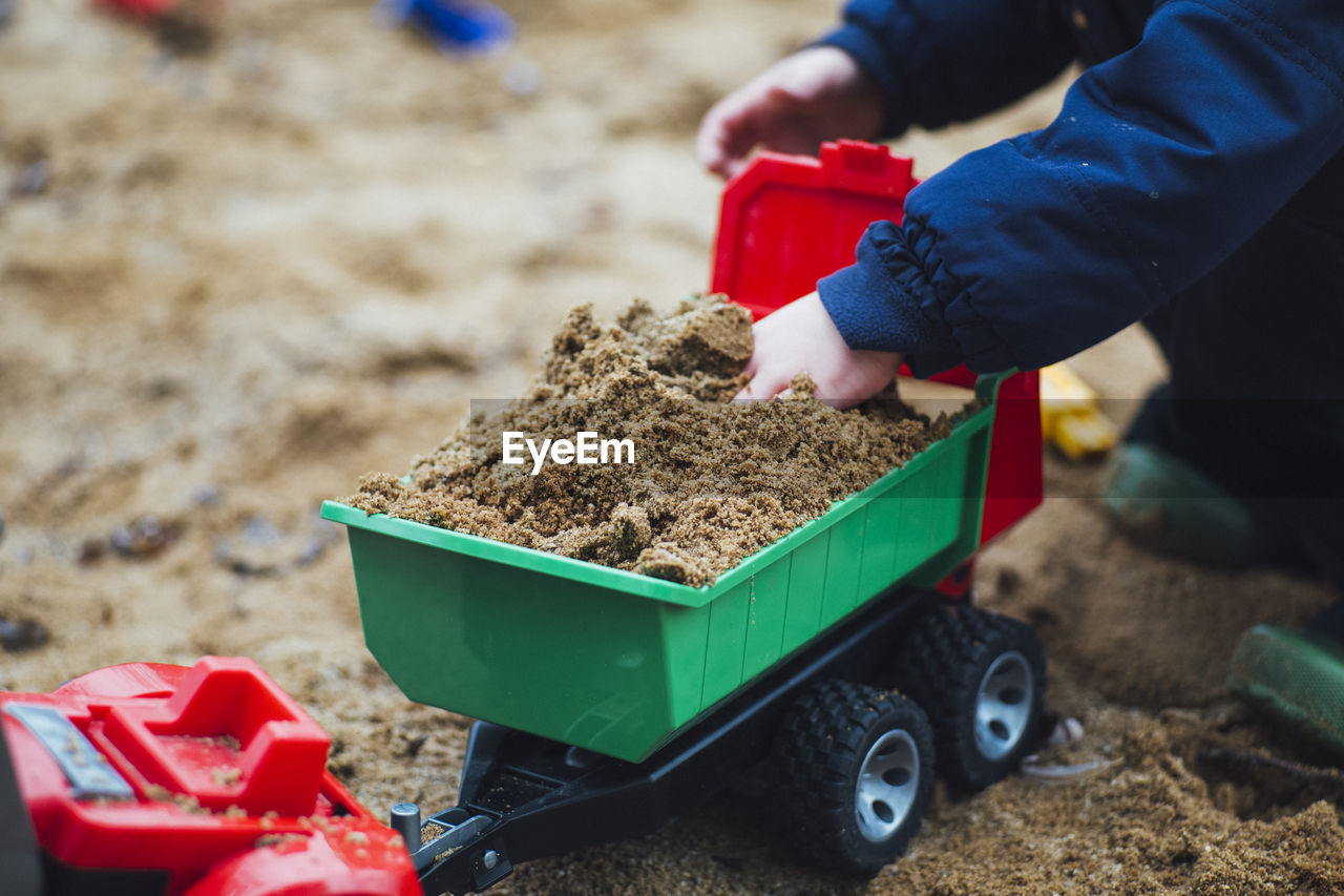 Cropped image of kid playing with toy truck on sand at beach