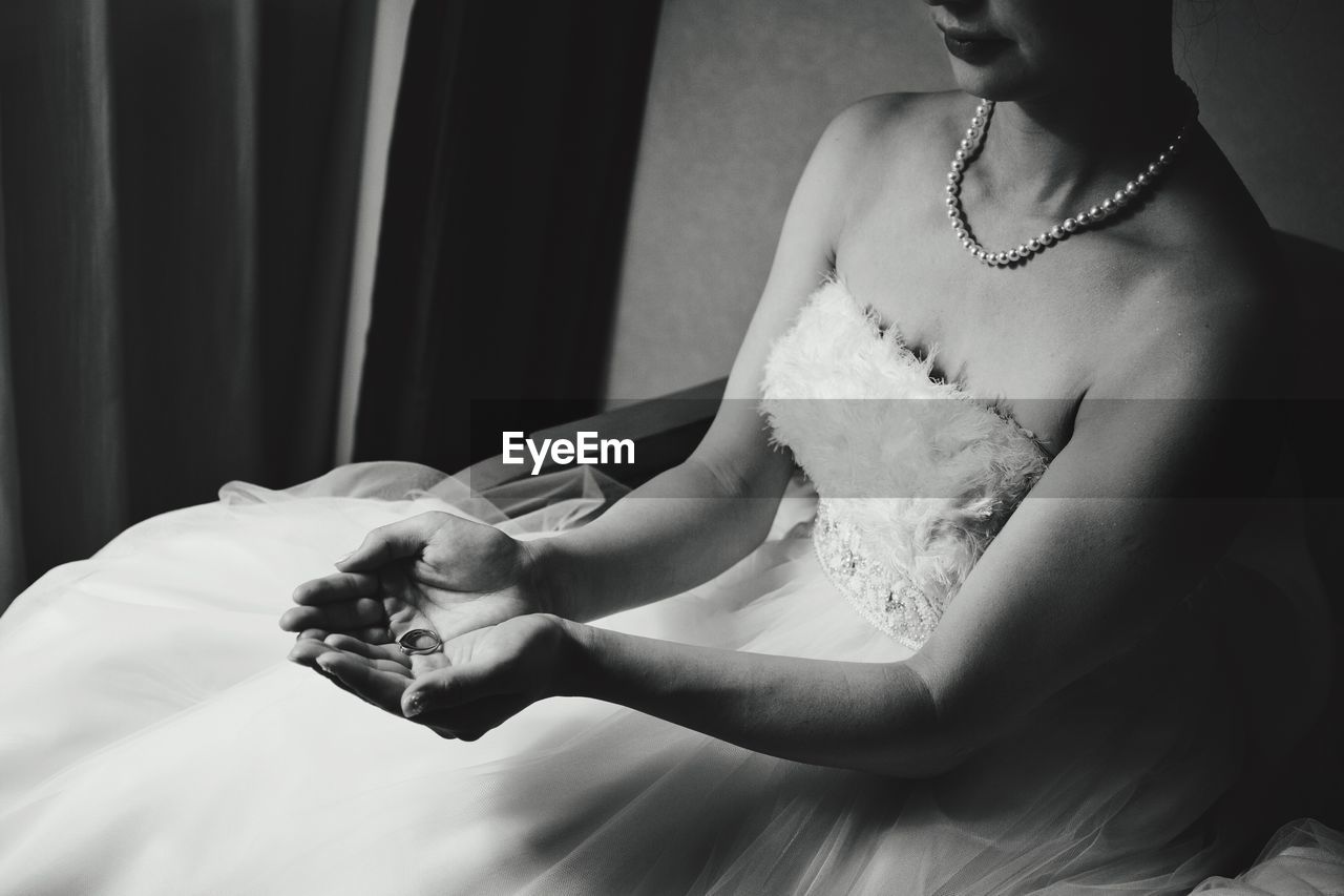 Midsection of bride wearing wedding dress holding ring while sitting on chair