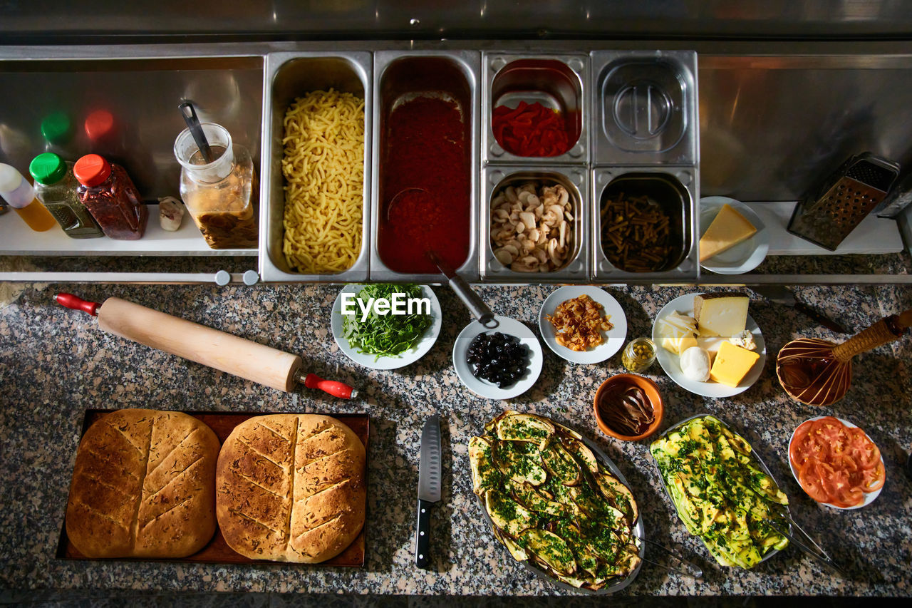 Top view of baking tray with hot freshly baked focaccia bread on marble table with various ingredients in restaurant kitchen