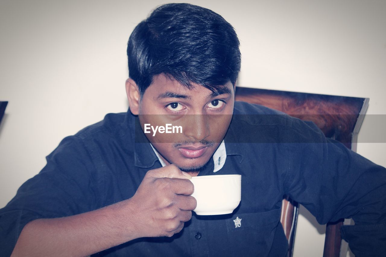 PORTRAIT OF YOUNG MAN USING MOBILE PHONE IN OFFICE