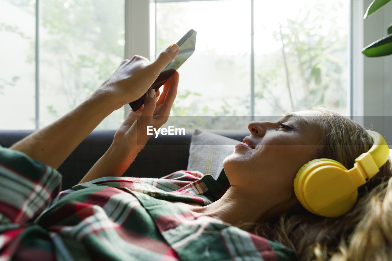 Woman using smart phone listening to music through headphones at home