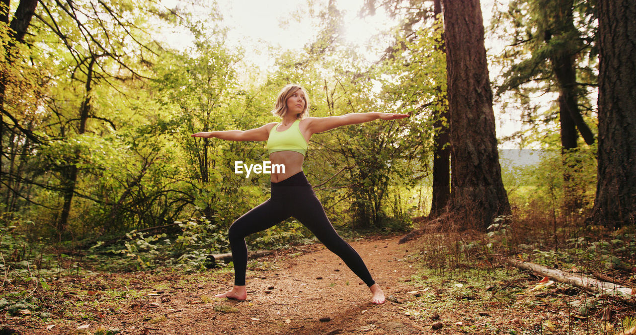 Full length of young woman with arms outstretched exercising in forest