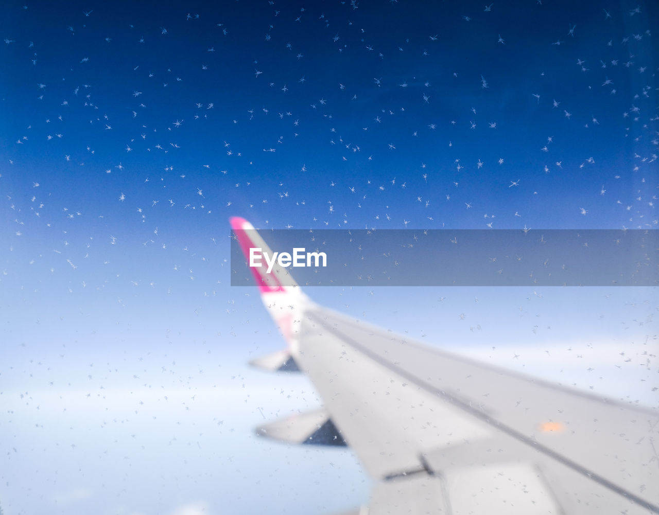 Aircraft wing seen through glass window against blue sky