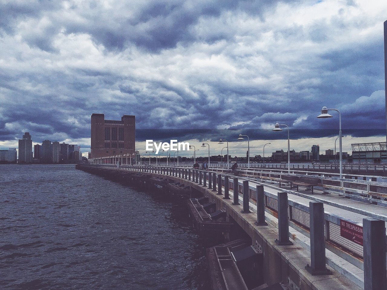 Bridge over river in city against cloudy sky