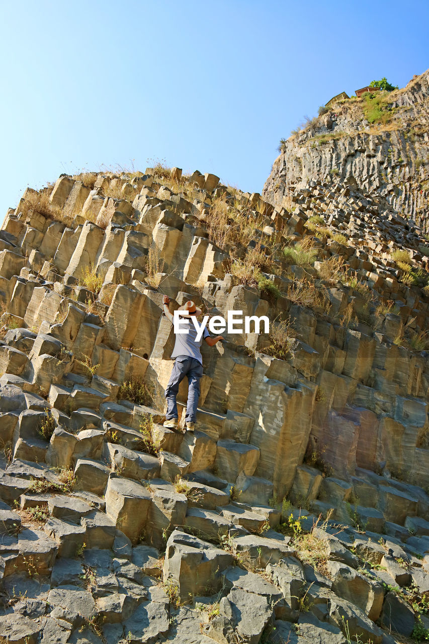 Traveler climbing symphony of stones, massive basalt rock formations along garni gorge in armenia