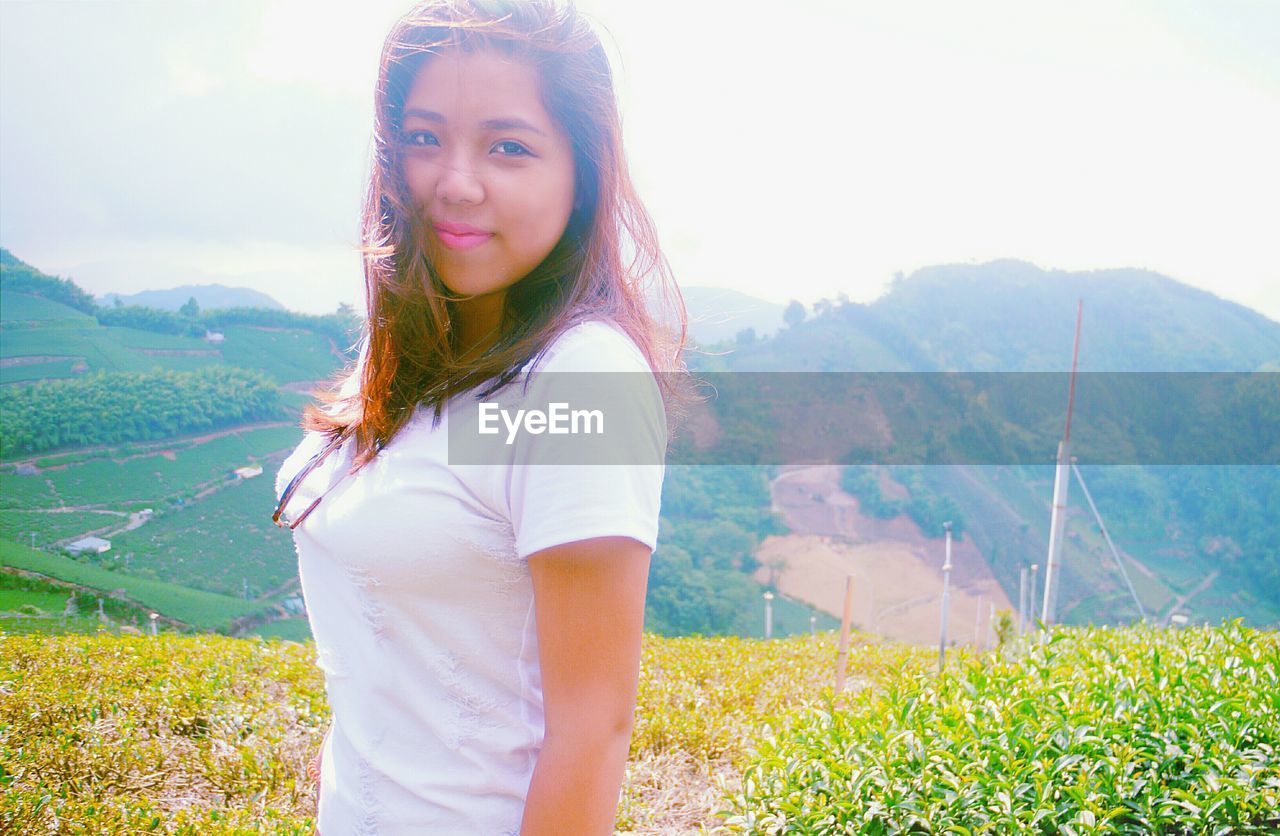 Portrait of smiling woman standing on hill against sky