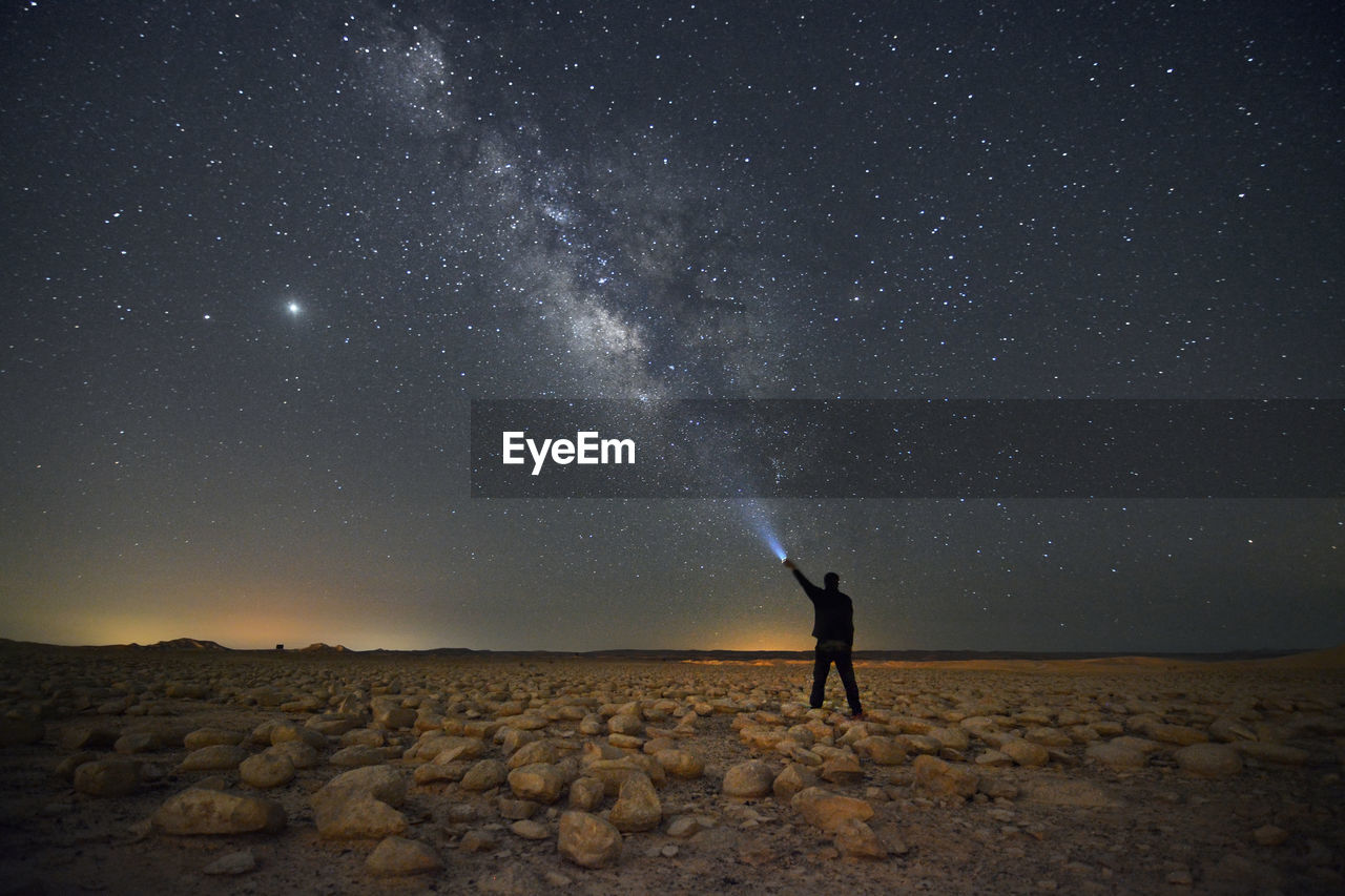 A man with a flashlight standing in the desert and the milky way
