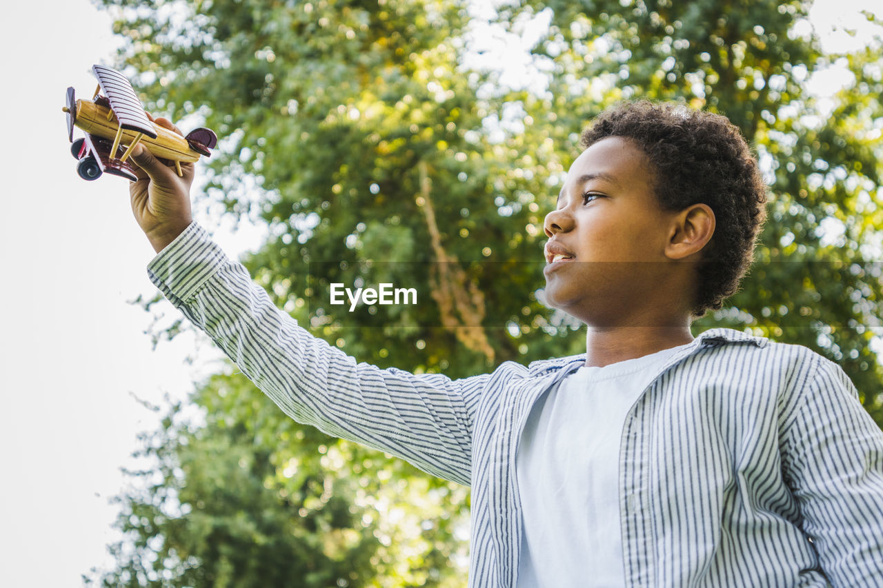 side view of young woman with arms outstretched standing against trees