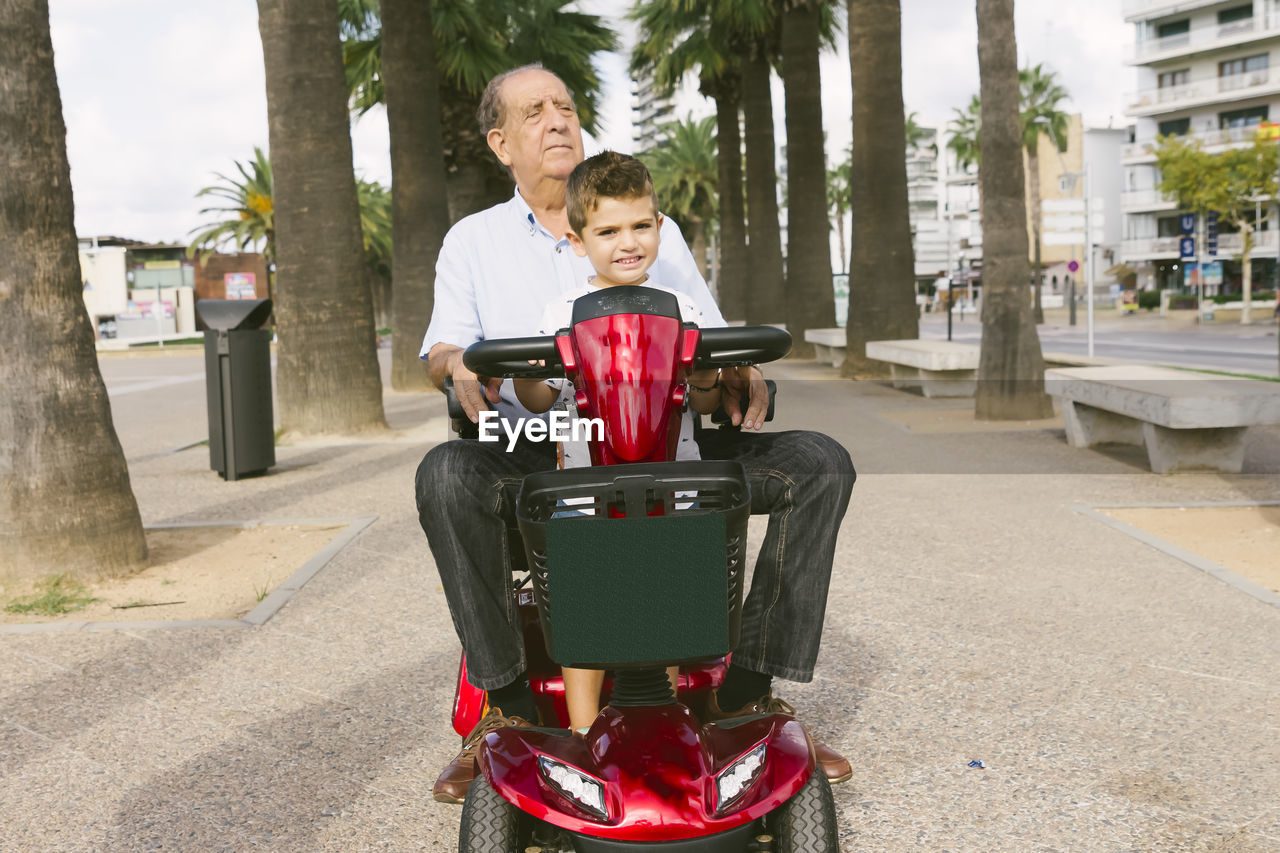 Grandfather riding grandson while sitting against trees on footpath