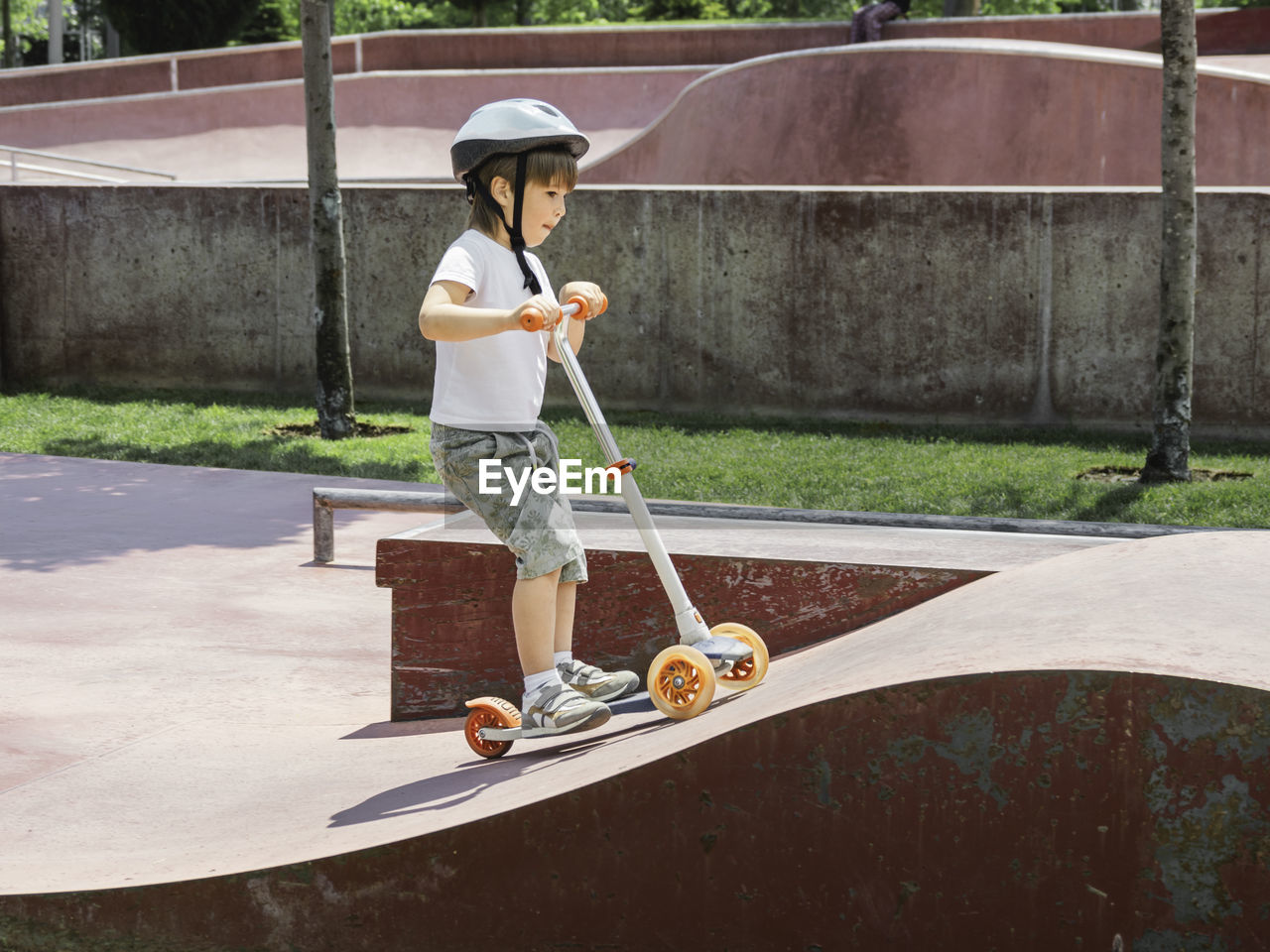 Little boy rides kick scooter in skate park. special concrete bowl in urban park. training to skate.