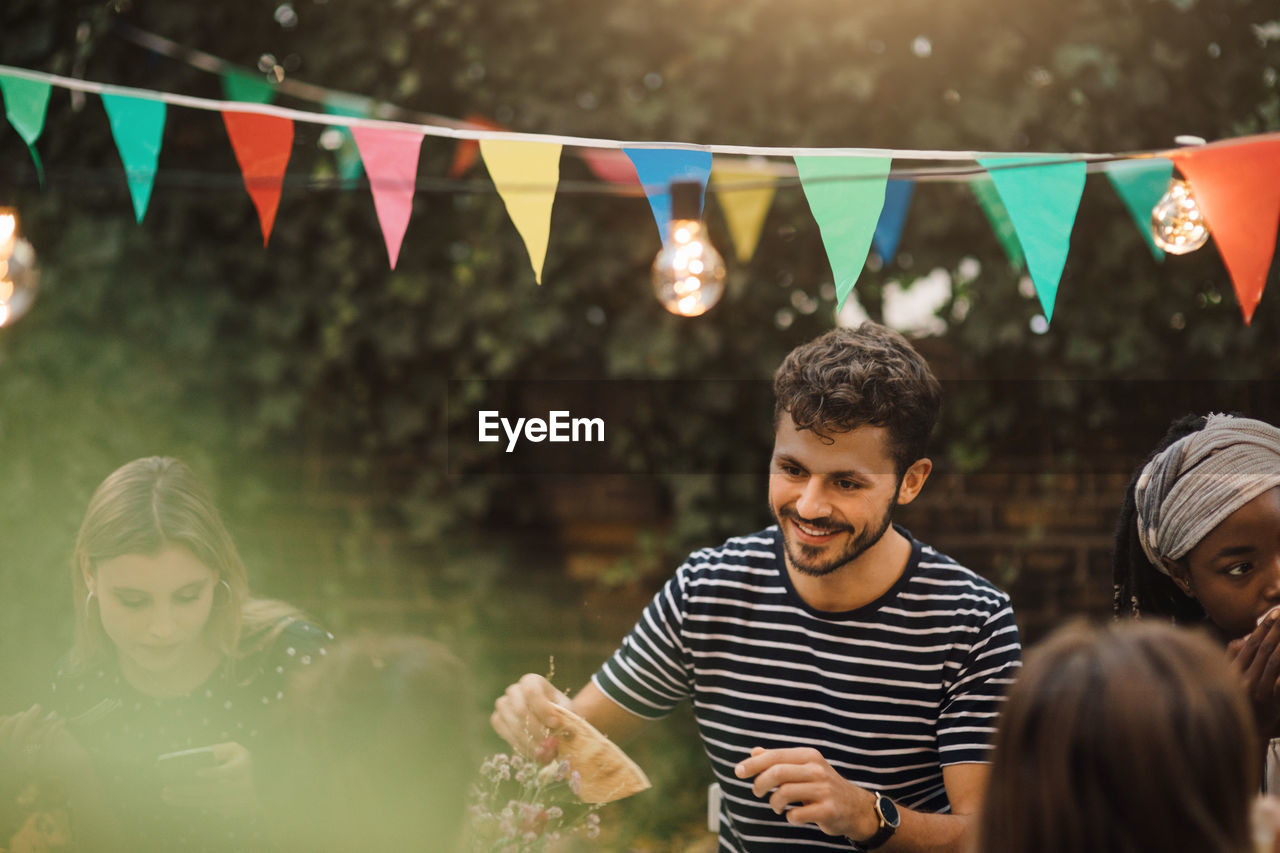 Smiling young man enjoying dinner party with friends in backyard