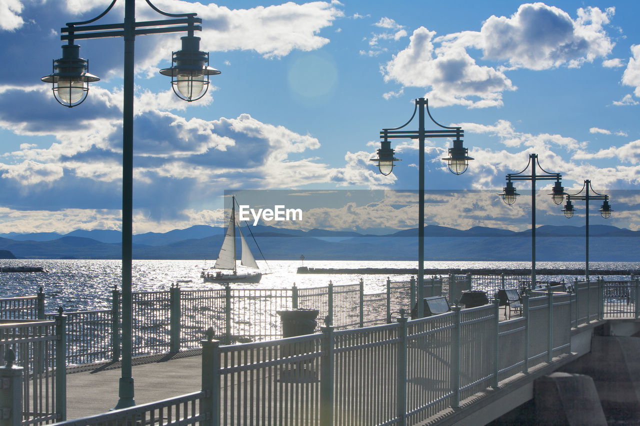 sky, cloud, water, street light, architecture, nature, transportation, sea, railing, travel destinations, city, built structure, travel, lighting equipment, nautical vessel, tourism, street, ship, no people, dock, building exterior, mode of transportation, day, vehicle, outdoors, scenics - nature, mountain, beauty in nature, vacation, holiday, sunlight, marina, pier, cityscape, trip, blue, harbor