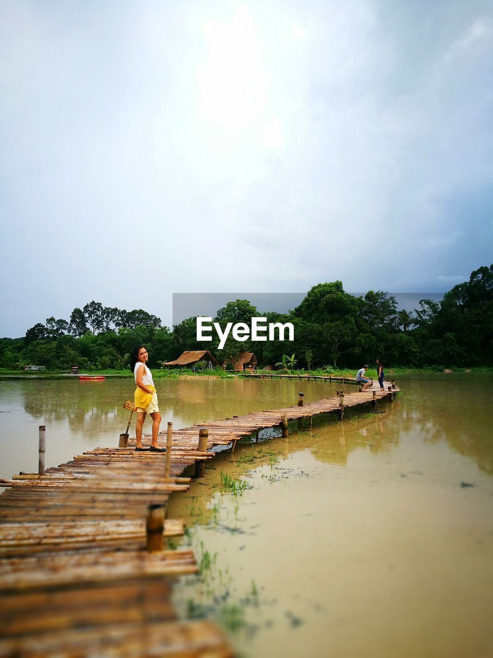 Woman standing on footbridge over lake against sky