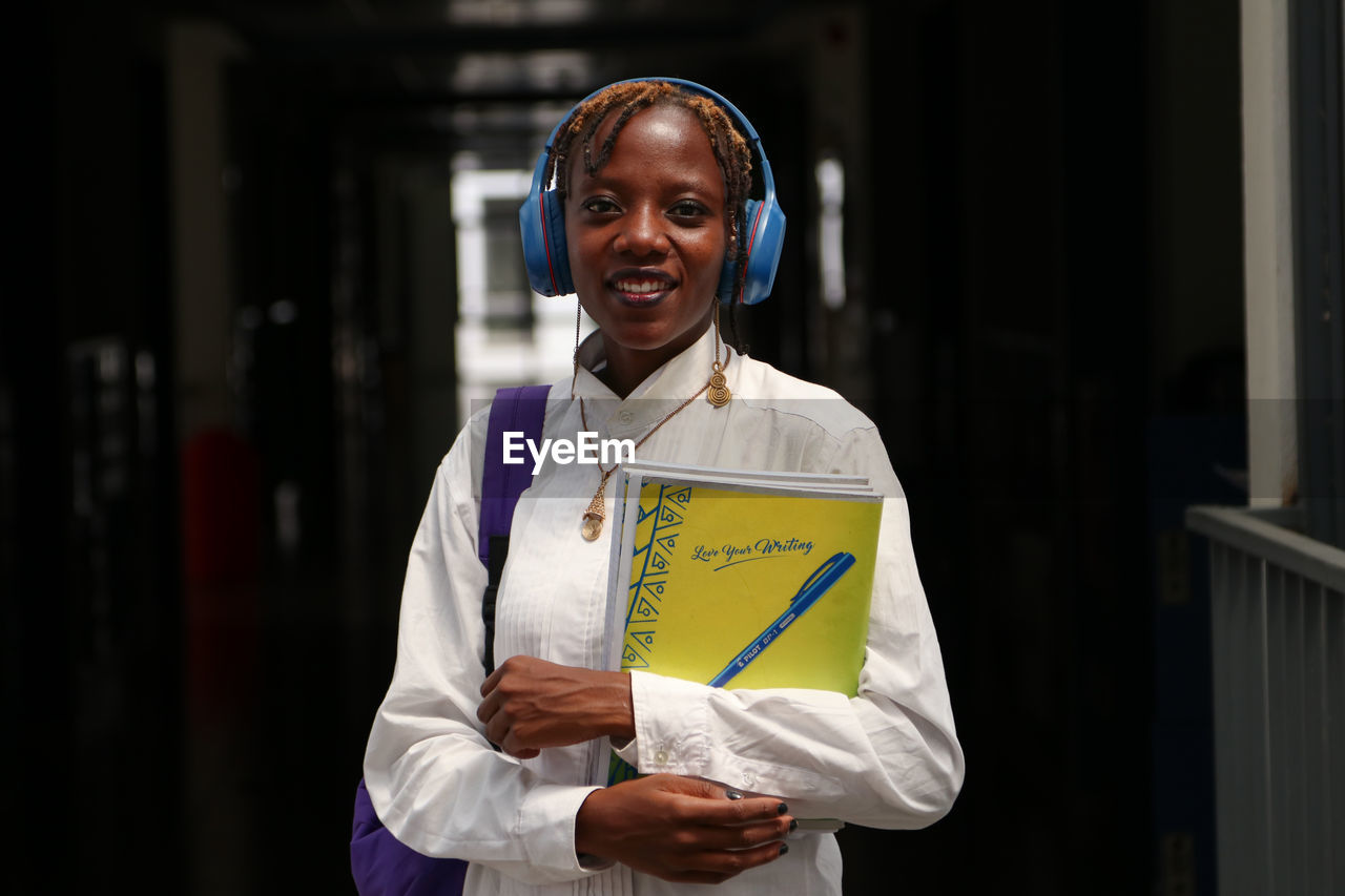 Portrait of a smiling pretty young female african student holding books and wearing headphones