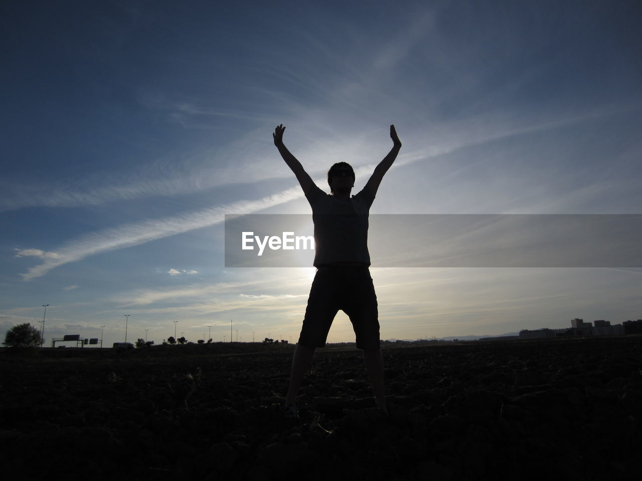 Silhouette man standing with arms raised on field against sky