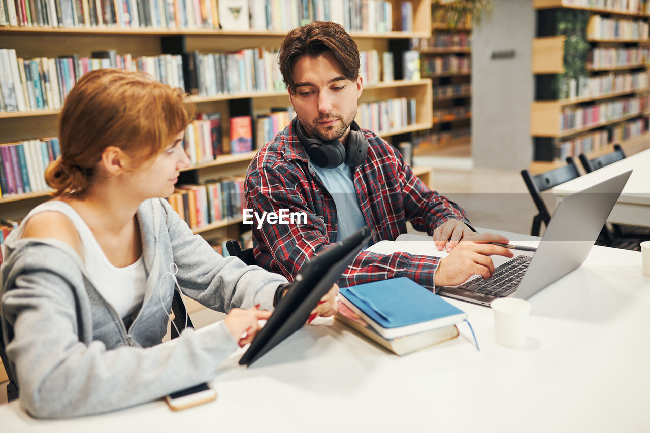 Students learning in university library. young man preparing for test on laptop. girl writing essay