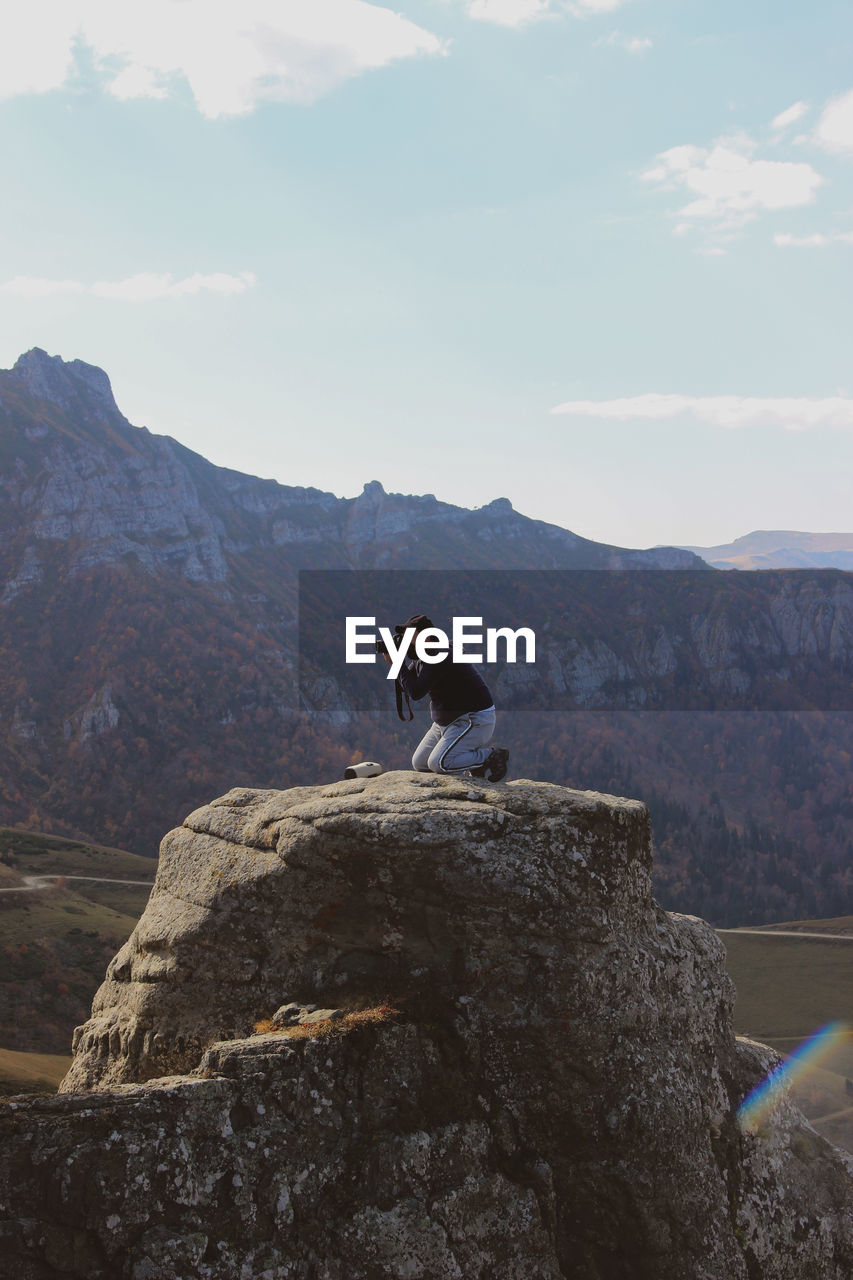 MAN STANDING ON ROCK AGAINST MOUNTAIN RANGE