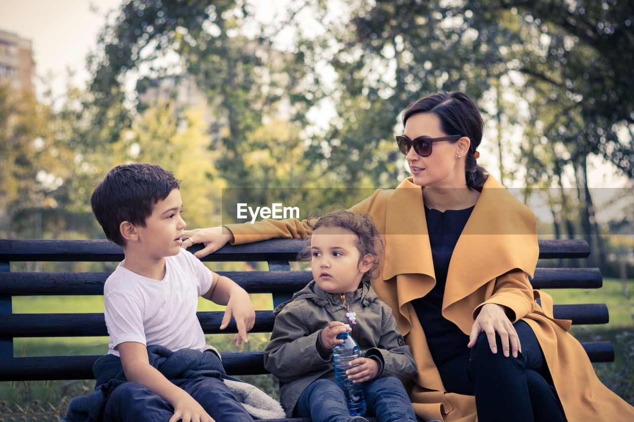 Family sitting on bench against trees at park