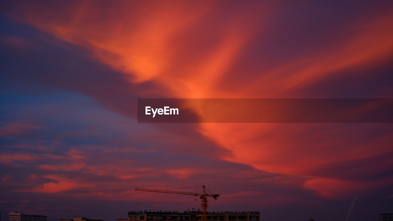 LOW ANGLE VIEW OF SILHOUETTE CRANES AGAINST ORANGE SKY
