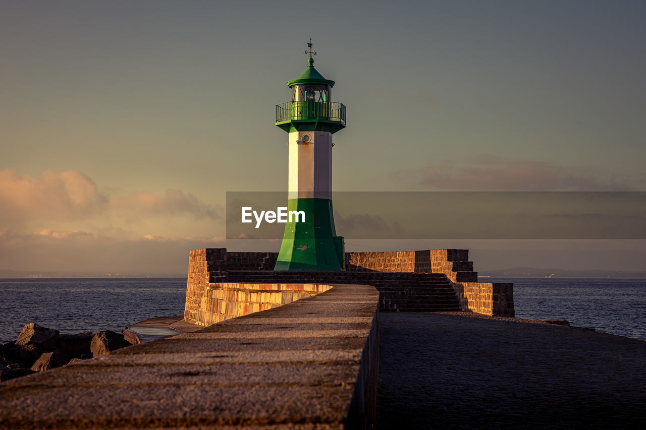 Lighthouse by sea against sky during sunset