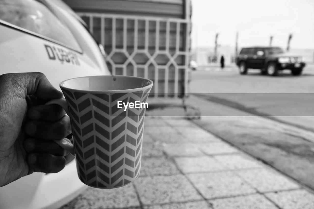 CLOSE-UP OF HAND HOLDING COFFEE CUP WITH SPOON