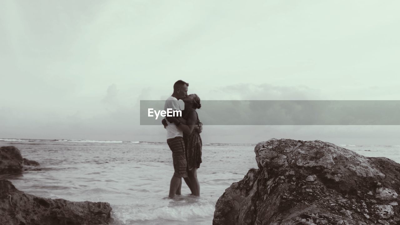 Couple kissing while standing in sea against sky