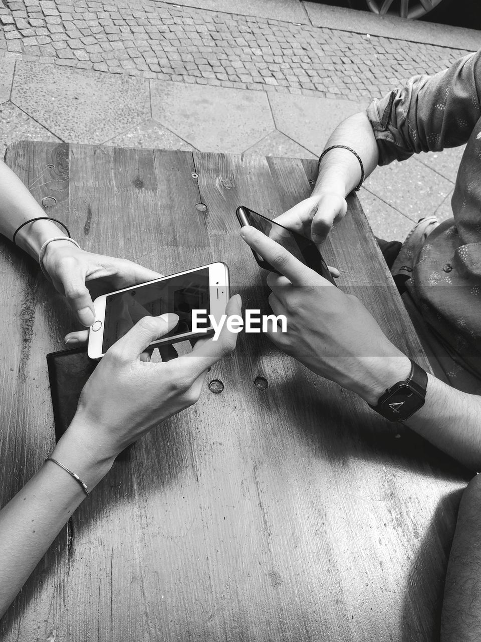 CLOSE-UP OF HANDS HOLDING MOBILE PHONE ON TABLE