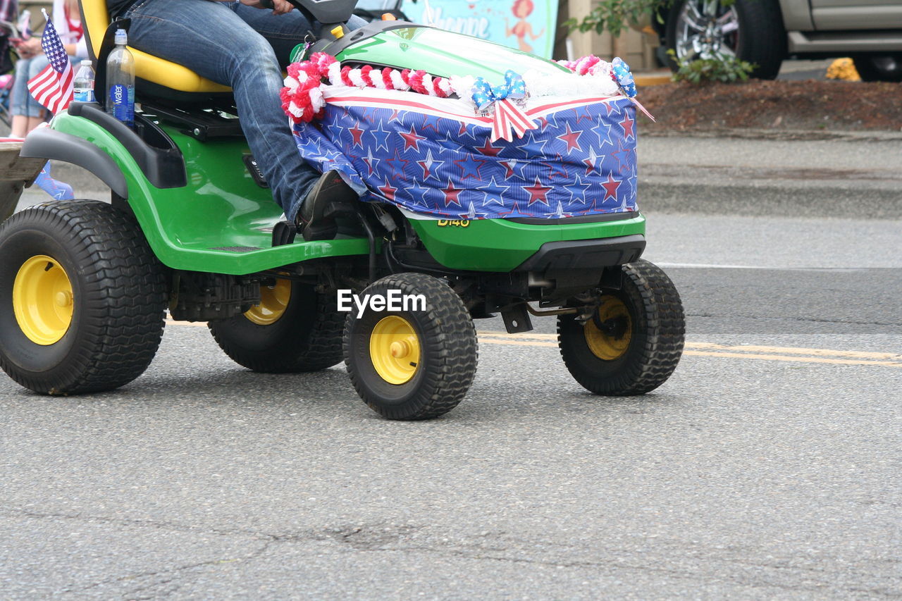 Low section of men riding tractor at street on fourth of july independence day parade