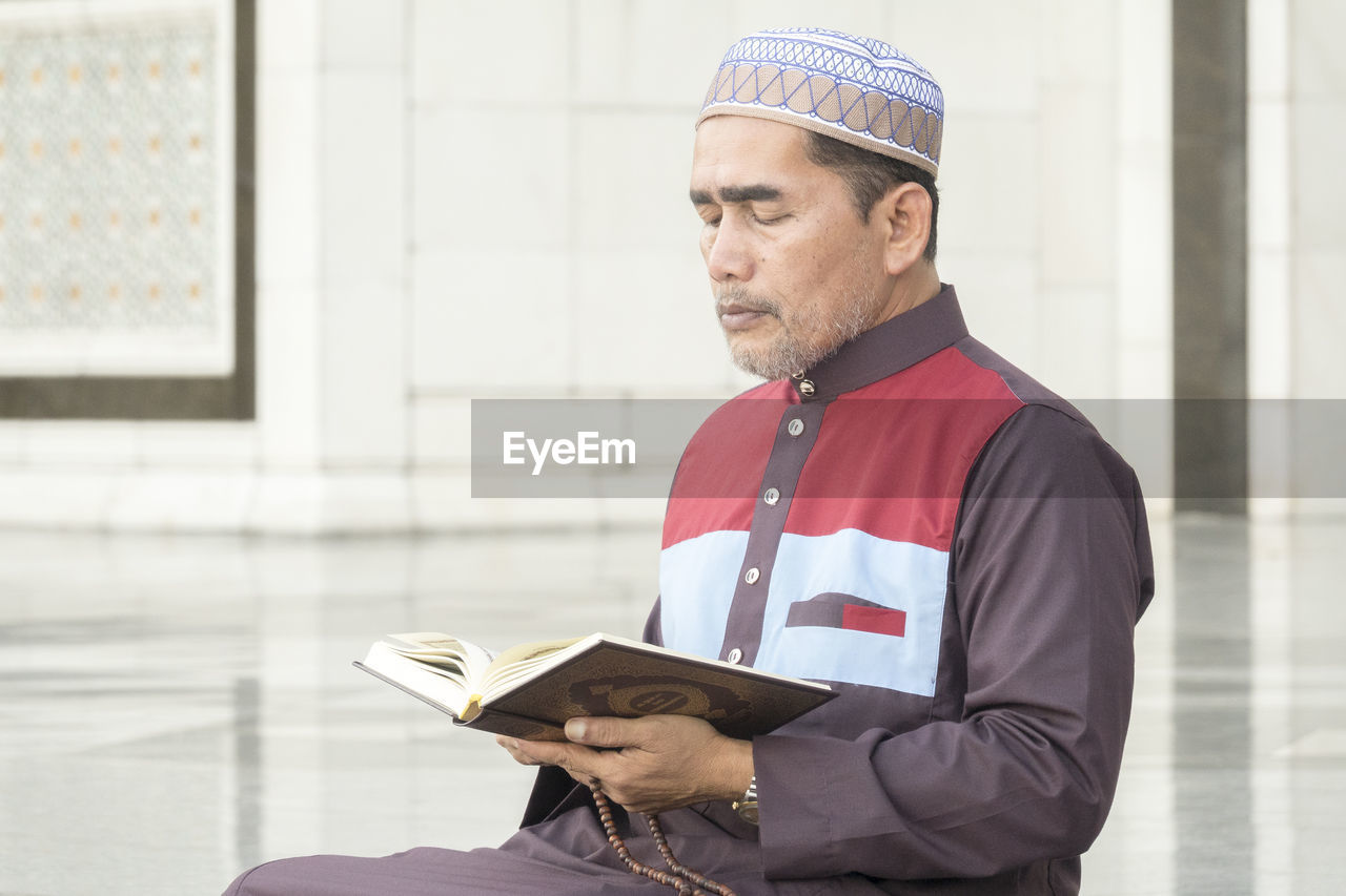 Mature man reading koran while sitting at mosque