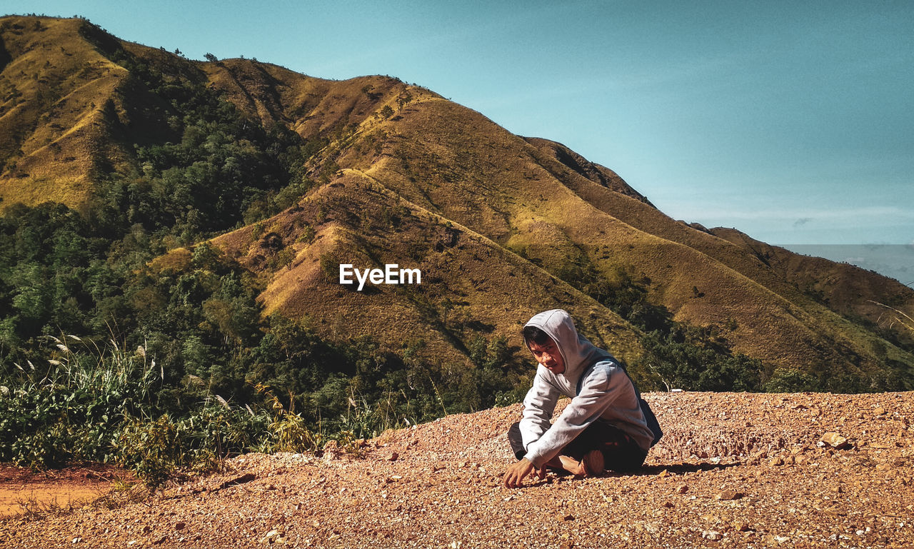 Portrait of young man sitting on field against mountain