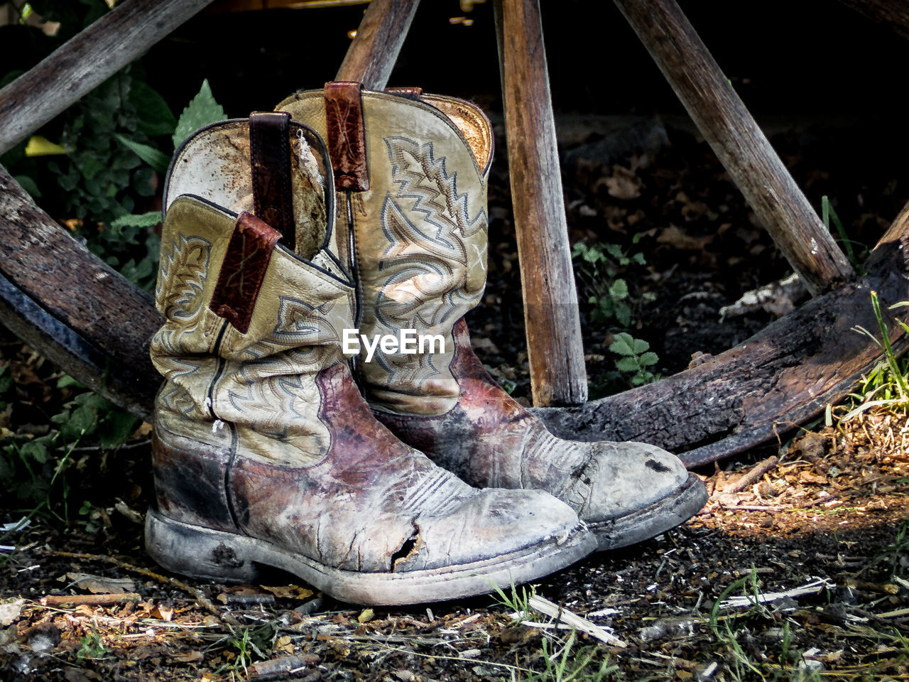 Close-up of boots by wooden wheel