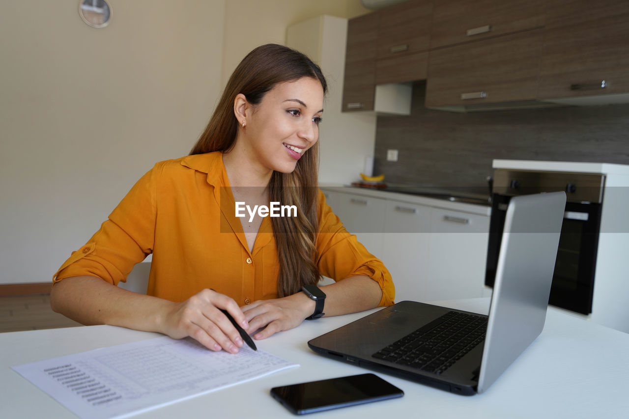 Brazilian girl working at home filling out documents communicating through video conference