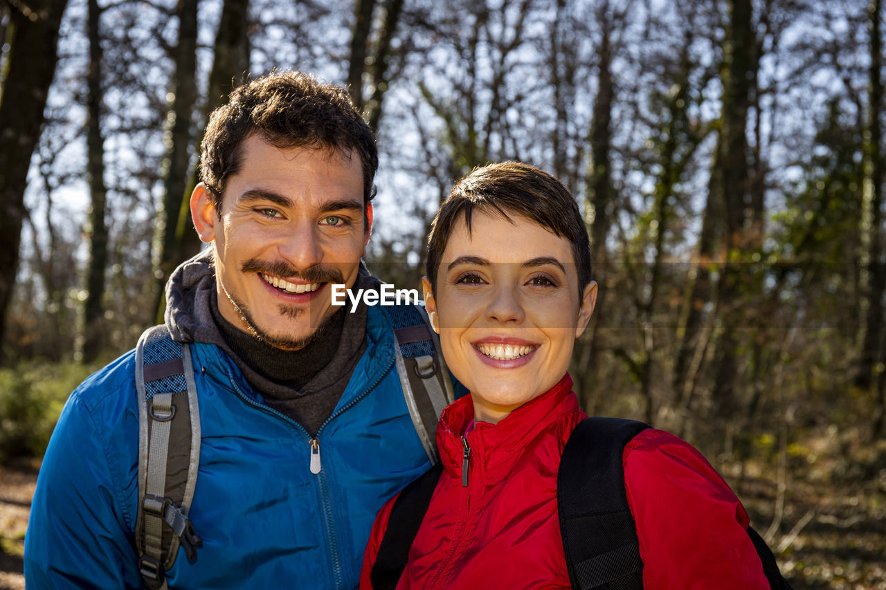 Beautiful young couple is hiking in the woods. the smiling couple looks into the camera.