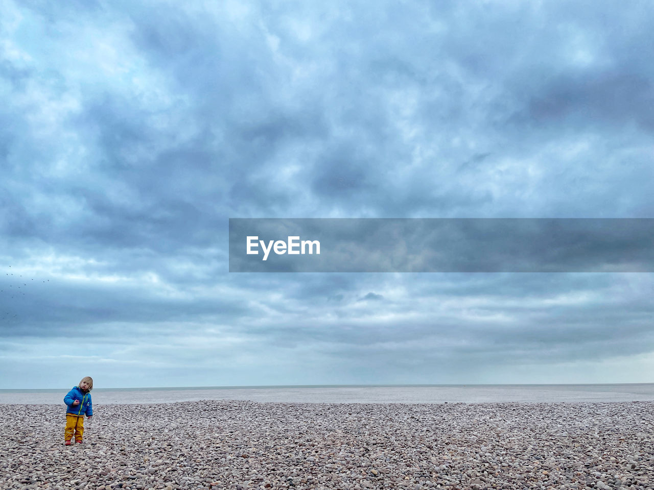 REAR VIEW OF MAN STANDING AT BEACH AGAINST SKY