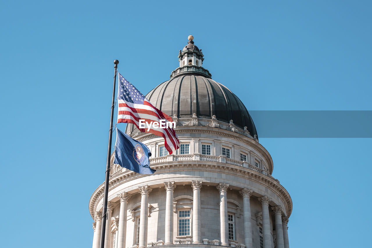 American flag waving at state capitol building with blue sky in background