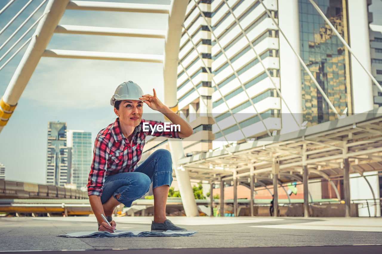 Female engineer working on blueprint while standing in city