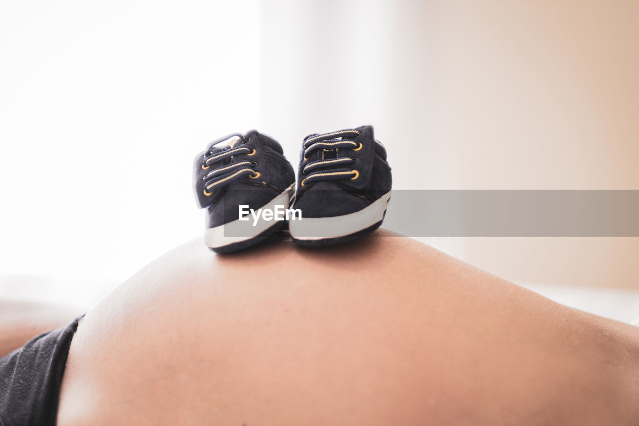 Midsection of pregnant woman with baby shoes on top at home