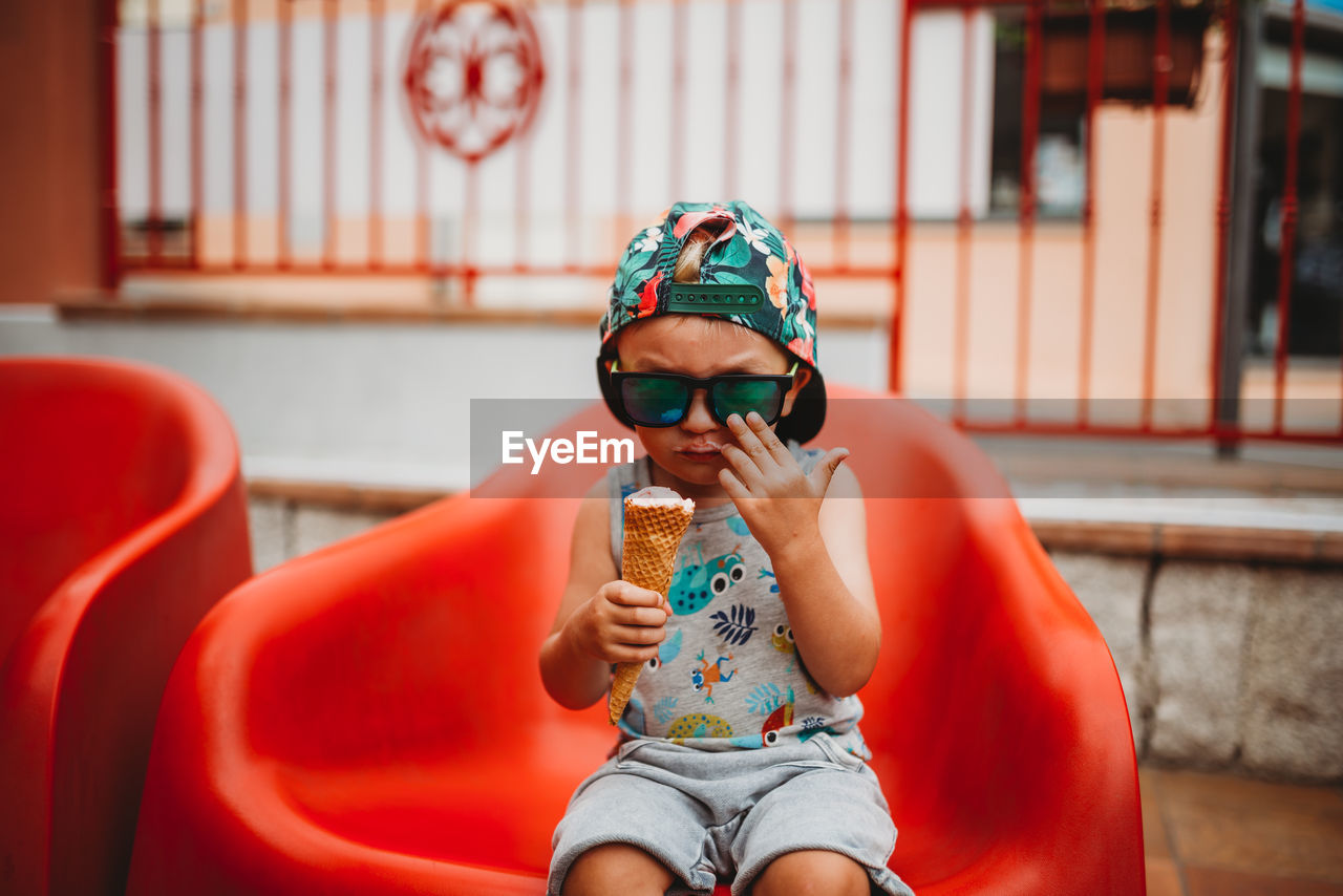 White male toddler eating ice cream with sunglasses and cap to back