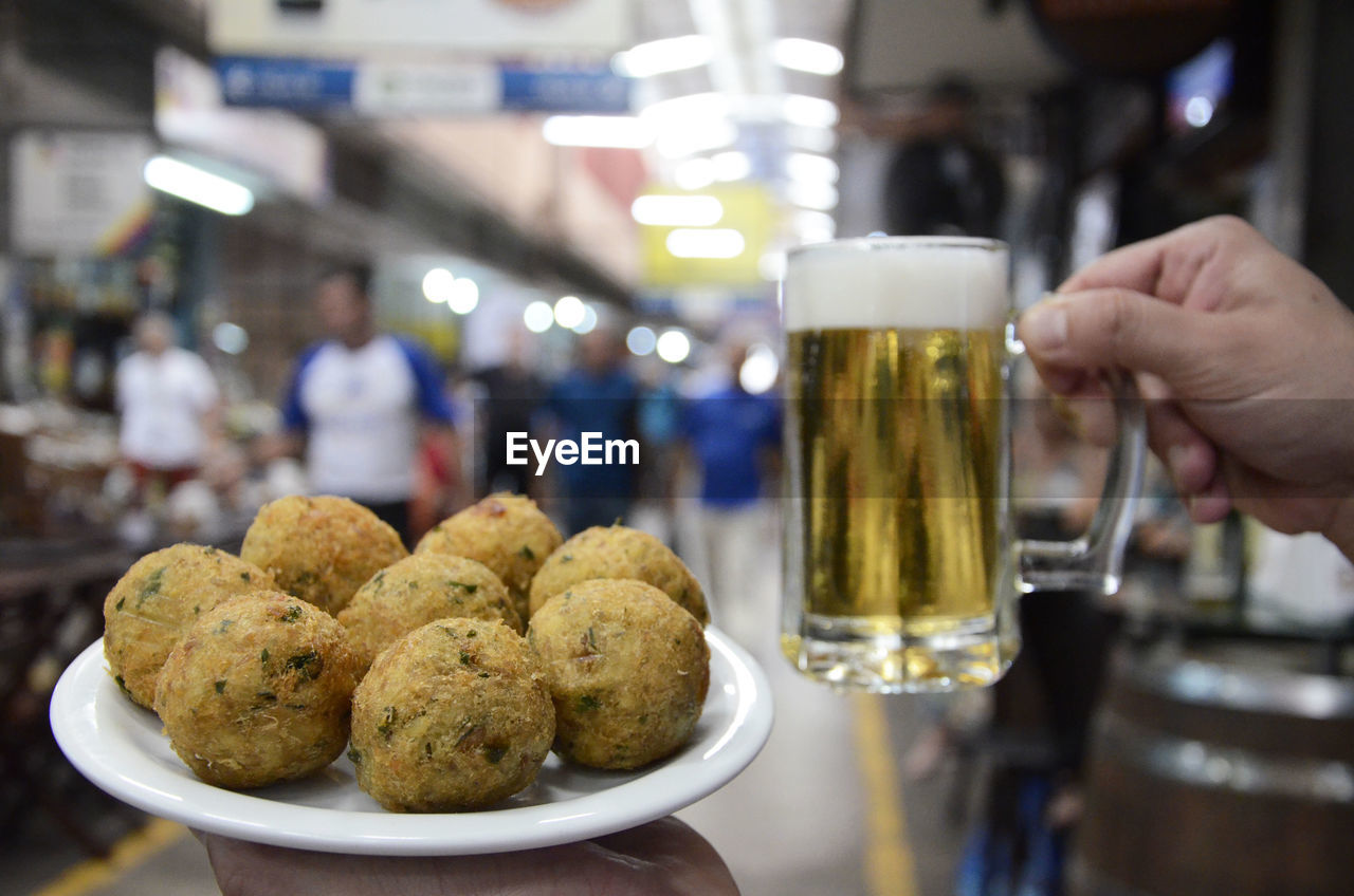 Cropped image of person holding meatballs and beer in market