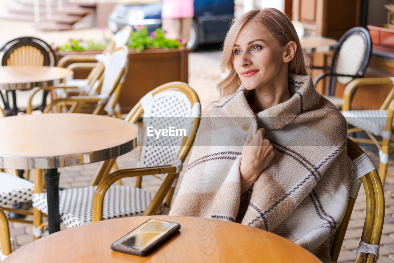 Young woman while relaxing in cafe at table on street, happy caucasian woman