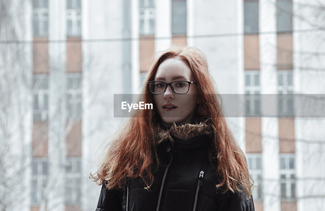 Portrait of beautiful young woman standing against building in city