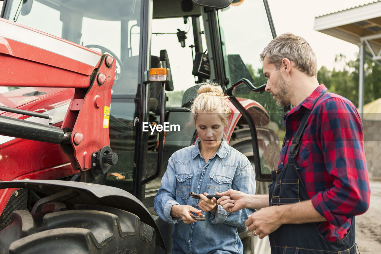 Man and woman holding equipment while standing by tractor at farm