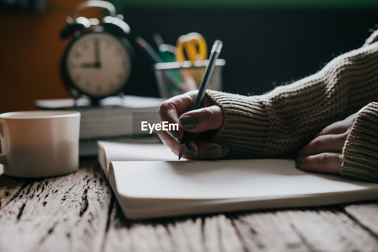 Cropped image of woman writing on book by coffee cup on table