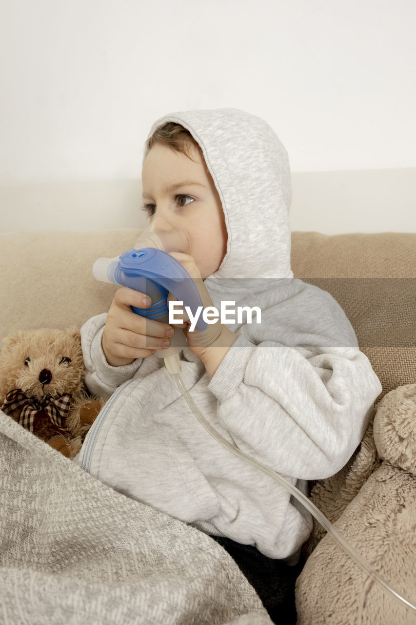 Sick little boy with inhaler for cough treatment. unwell kid doing inhalation on his bed. flu season