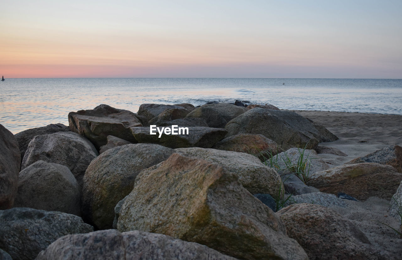 Rocks on beach against sky during sunset