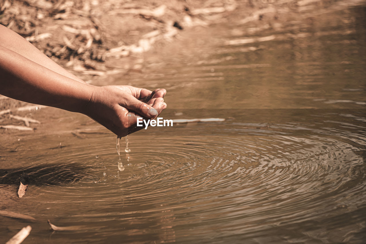 Cropped image of hands holding water by lake