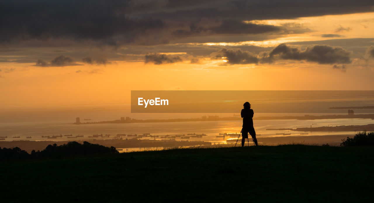 Silhouette man standing on field against sky during sunset